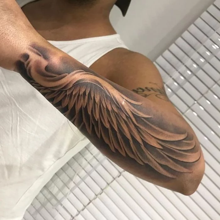 angel wings tattoo, arm tattoo, man with white top, white blinds in the background