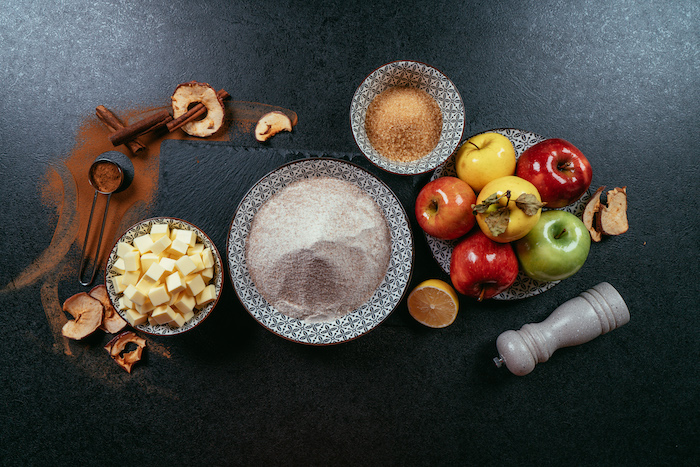 different ingredients in different bowls, red green and yellow apples on black and white plate, apple pie recipe