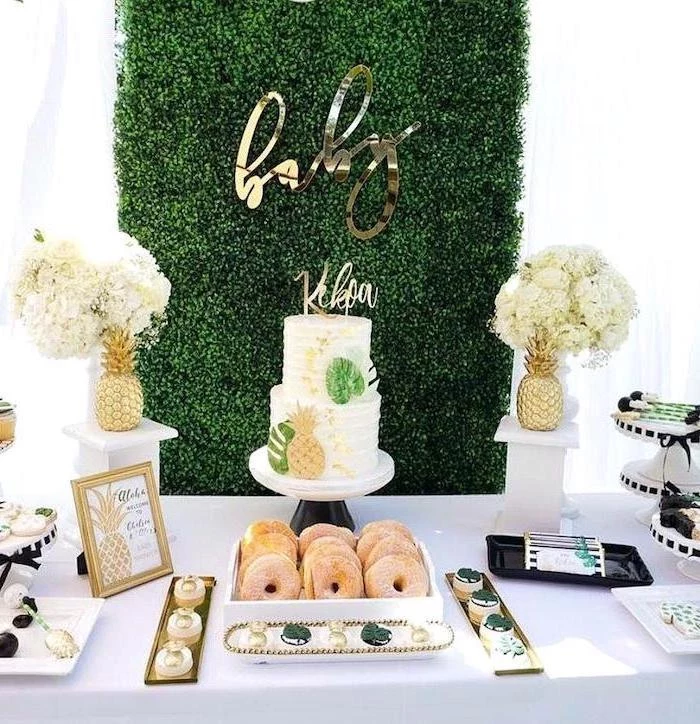 greenery wall, two tier cake, donuts and cupcakes, flower bouquets, baby shower decoration ideas, pineapples theme