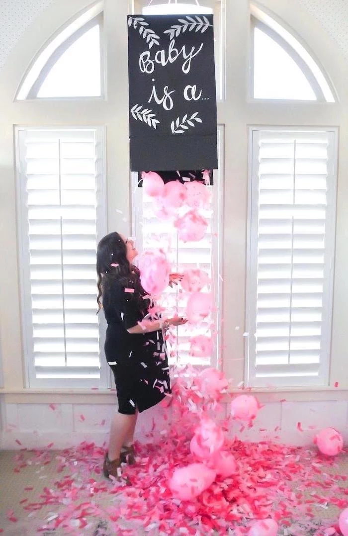 baby is a, black box, full of pink balloons, pink confetti, gender reveal party, woman standing underneath