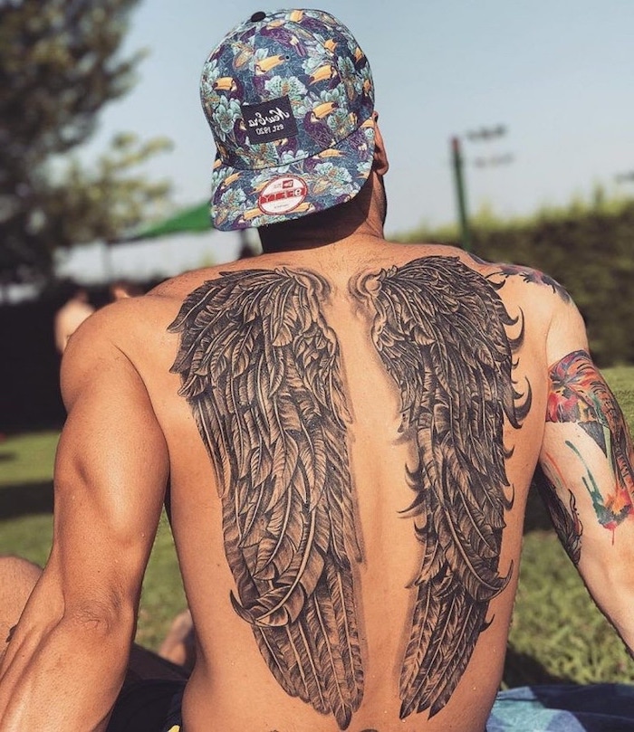 man with a floral hat, back tattoo, guardian angel tattoo, angel wings, blurred background