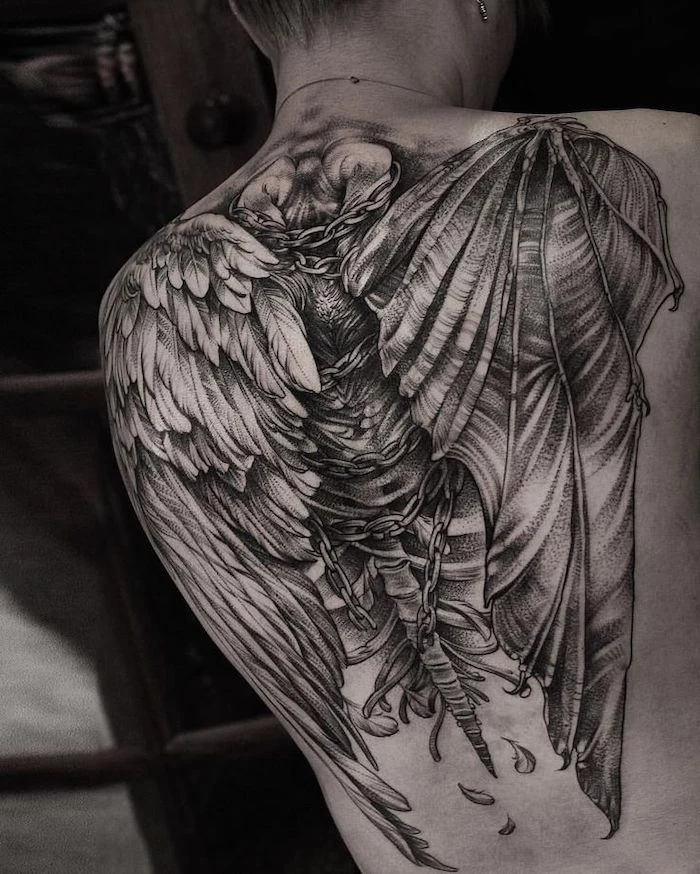 back tattoo, black and white photo, wings tattoo on back, one angel wing, one devil wing, tied with chains