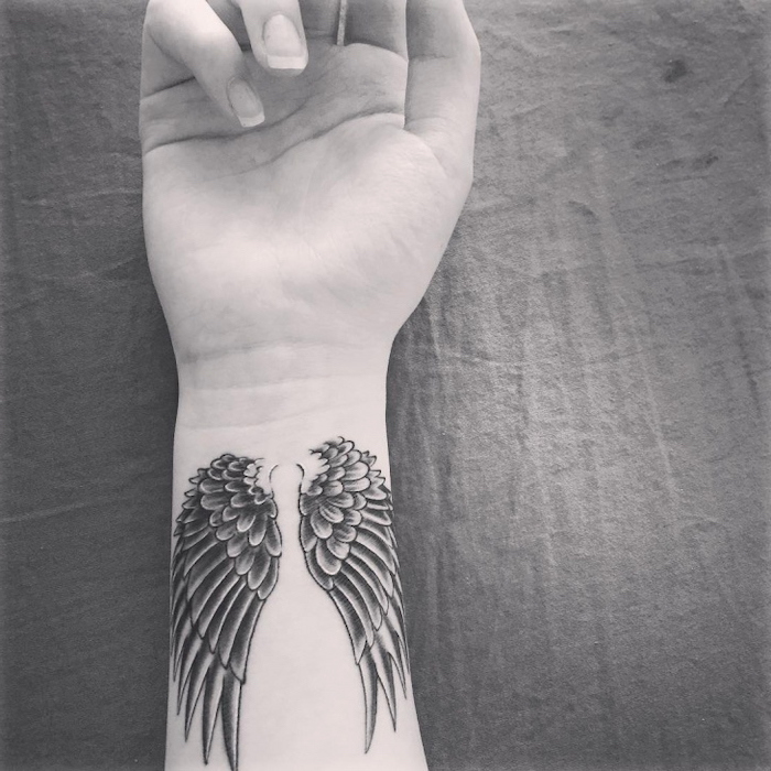 black and white photo, wings tattoo on back, wrist tattoo, grey background