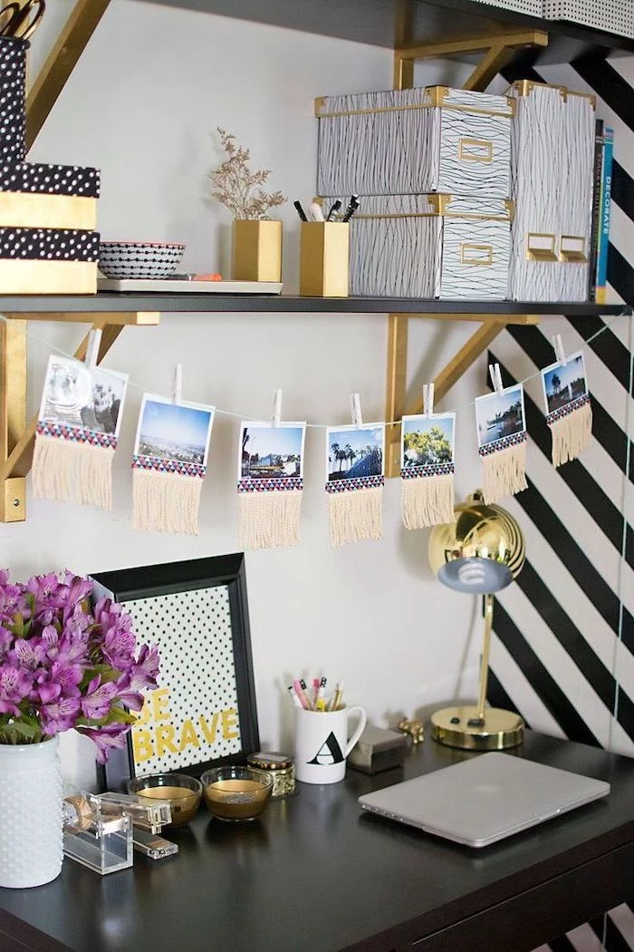 black desk, hanging photos above, wooden shelf, gold desk accessories, cubicle decor, purple flower bouquet