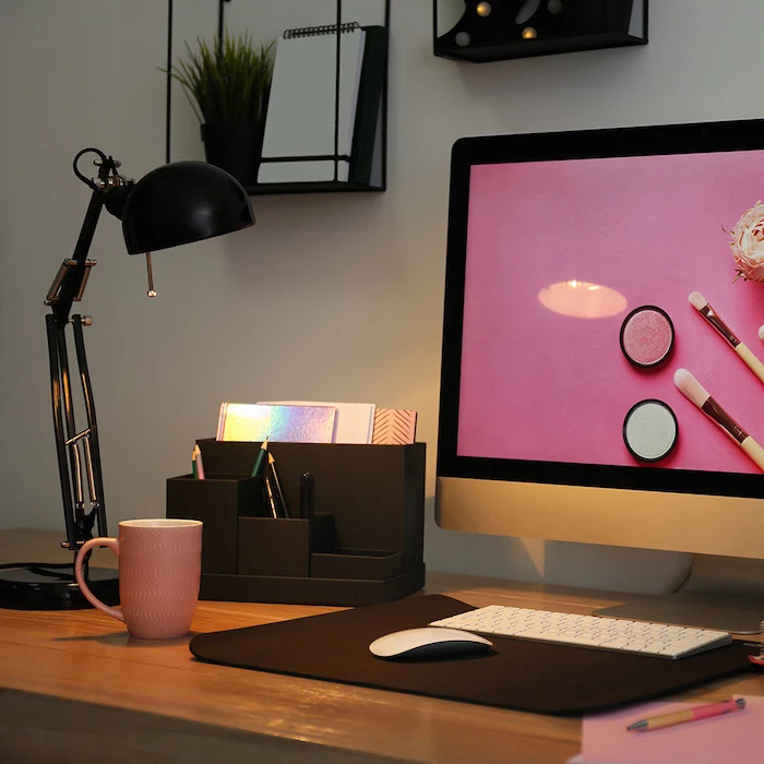 wooden desk, cubicle decor, black desk organiser, pink coffee mug, black metal shelves, desktop computer