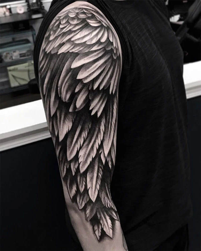 arm sleeve tattoo, small angel wings tattoo, man wearing a black top