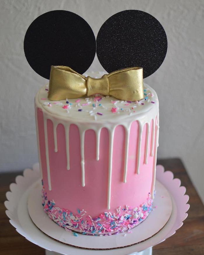 pink fondant, white frosting, minnie mouse 1st birthday cake, gold bow, colorful sprinkles, red and black minnie mouse cake