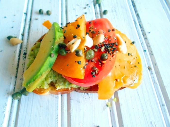 avocado toast, with sliced avocado and tomatoes, breakfast meals, capers on top, wooden table