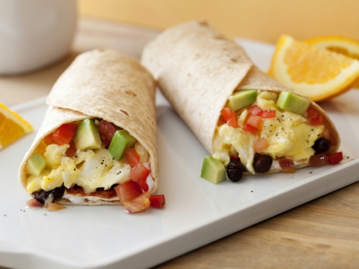 wrapped burritos, breakfast dishes, chopped avocado and tomatoes, eggs inside, on white board