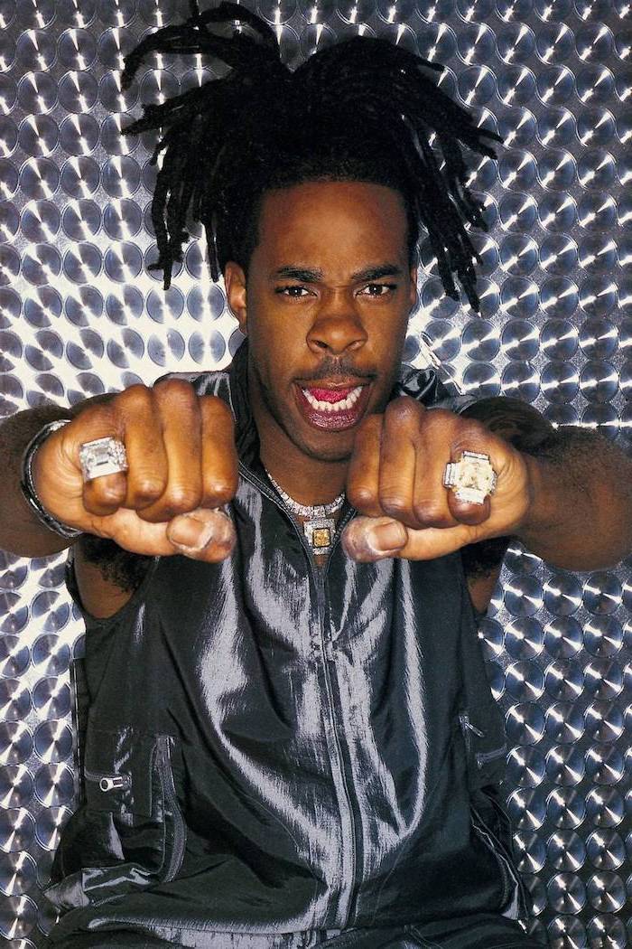 busta rhymes, wearing a gray top, diamond necklace, diamond rings, braided hair men, gray background