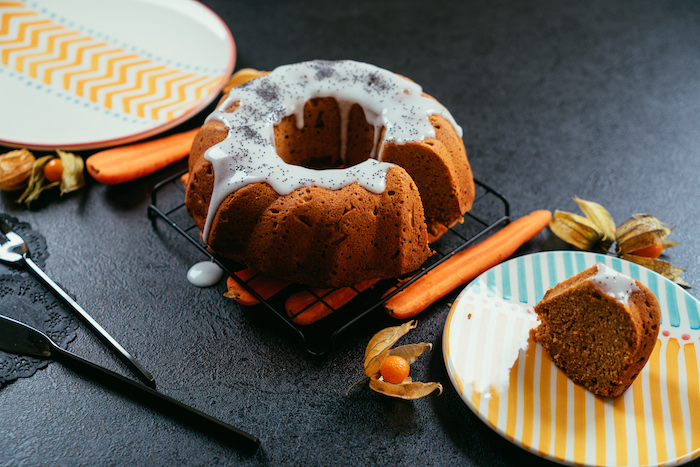 carrot cake with white icing, placed on metal rail, carrot cake recipe, piece of the cake on the side in a plate