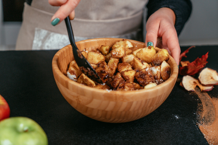 chopped apples mixed with cinnamon, in a wooden bowl with black spatula, apple pie recipe, by woman with green nail polish