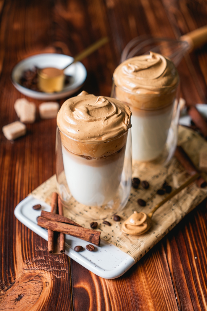 cloud coffee recipe, two glass cups, filled with milk and whipped coffee, cinnamon sticks and coffee beans around them