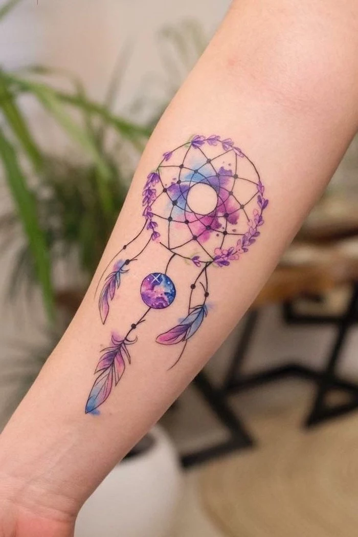 watercolor tattoo, dreamcatcher meaning, forearm tattoo, in purple blue and pink colors, blurred background, black and white dreamcatcher tattoo