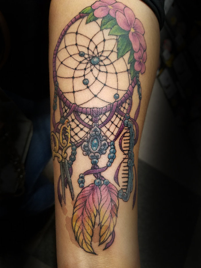 small dreamcatcher tattoo, colorful tattoo, back of arm tattoo, blurred background