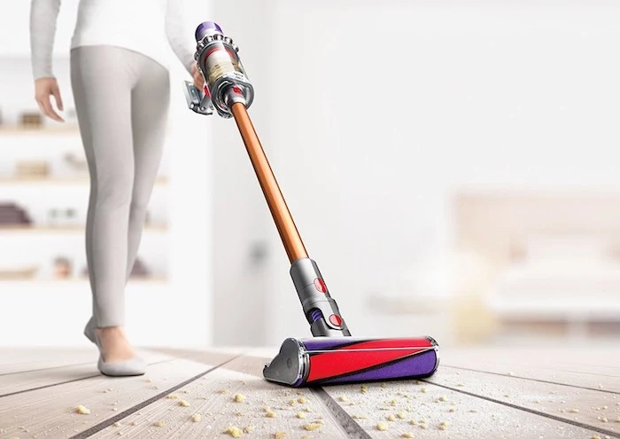 woman cleaning, wearing white blouse, gray trousers, wooden floor with breadcrumbs, best vacuum cleaner