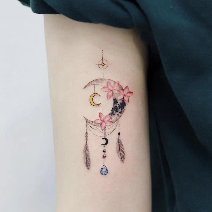 crescent moon, pink flowers, small dreamcatcher tattoo, back of arm tattoo, black shirt, white background