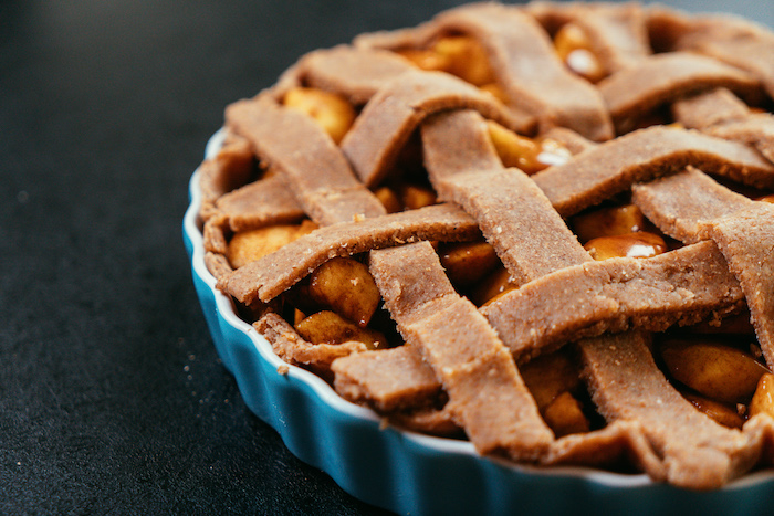 blue baking pan, apple pie recipe, crust and apples inside, placed on black surface