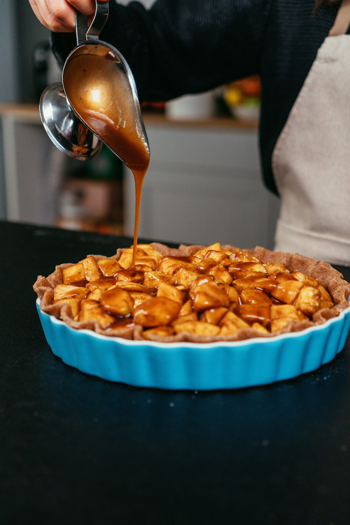 crust and apples placed in baking pan, caramel poured all over them, apple pie recipe, placed on black surface