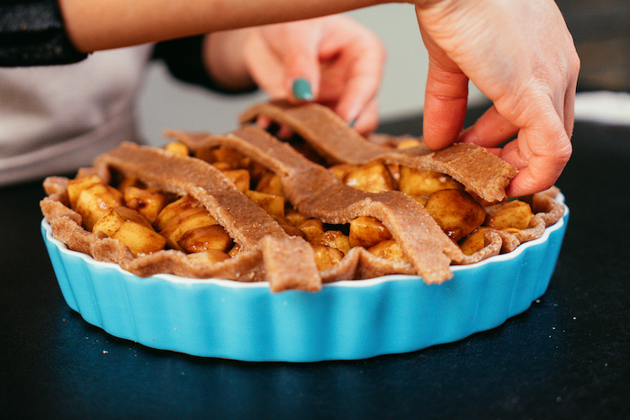 woman with green nail polish, putting top crust on the apple pie, placed in blue baking pan, apple pie recipe, placed on black surface