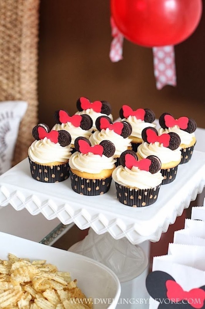 small cupcakes, minnie mouse birthday cake, white frosting, oreo ears, red bows, white cake stand