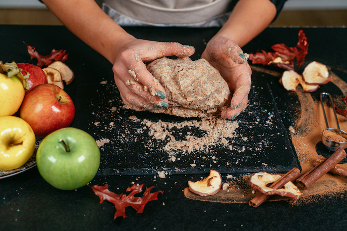 dough kneaded on black board, apple pie recipe, by woman with green nail polish, apples and cinnamon on the side