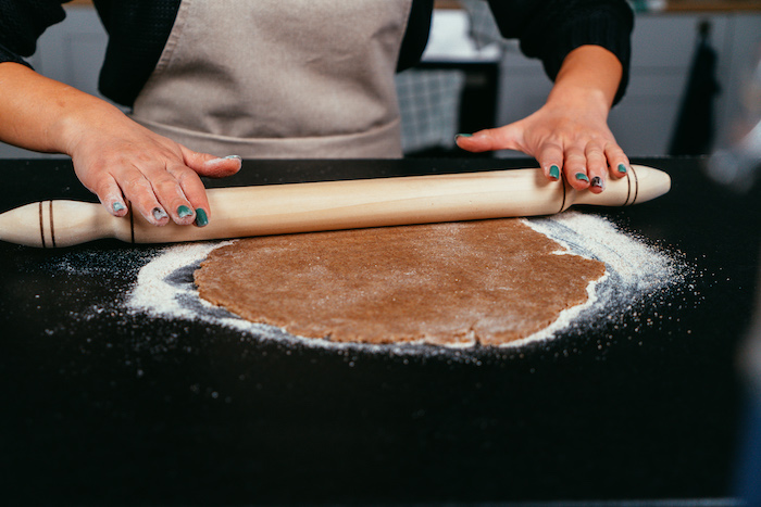 dough rolled out on lightly floured black surface, by a woman with green nail polish, apple pie recipe, wearing grey apron