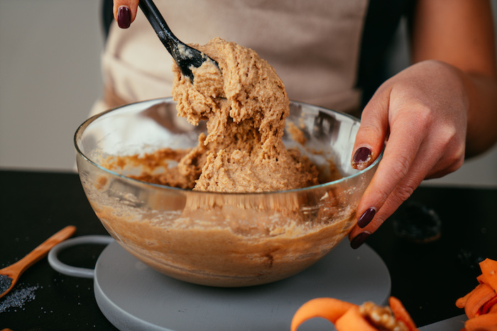 all ingredients mixed together in a glass bowl, carrot cake recipe, mixed with black spoon, placed on grey board