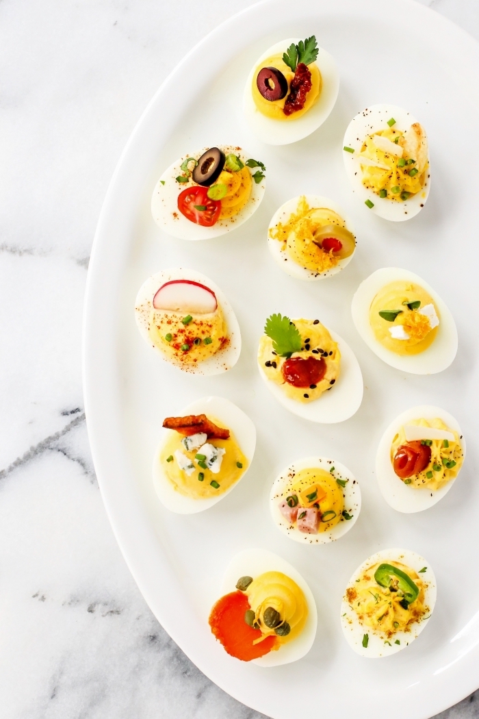 eggs with mayo inside, cherry tomatoes, peppers and olives, on white plate, breakfast brunch