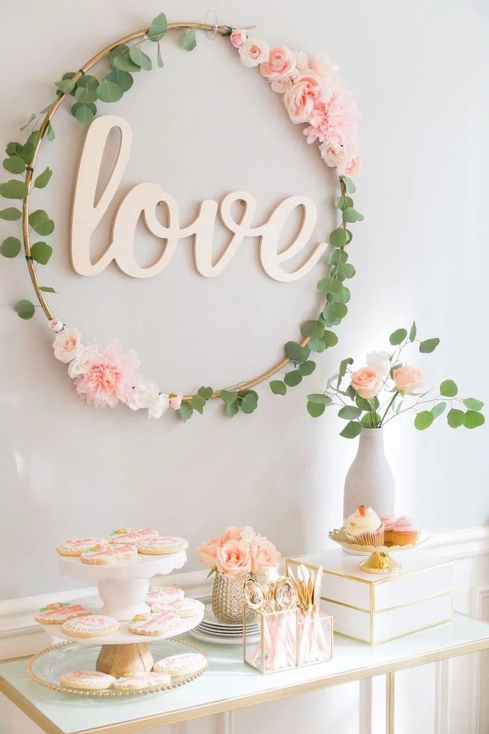 floral wreath, baby shower ideas, cake stand, cookies on it, small flower bouquets, love sign, white wooden table