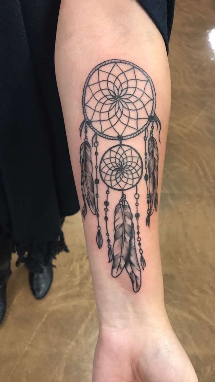 forearm tattoo, wolf dreamcatcher tattoo, woman with black dress, black shoes, brown floor