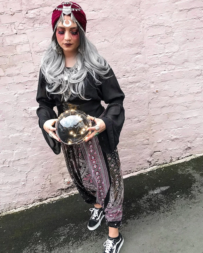 adult halloween costumes, woman with grey hair, dressed as a fortune teller, in front of a white brick wall
