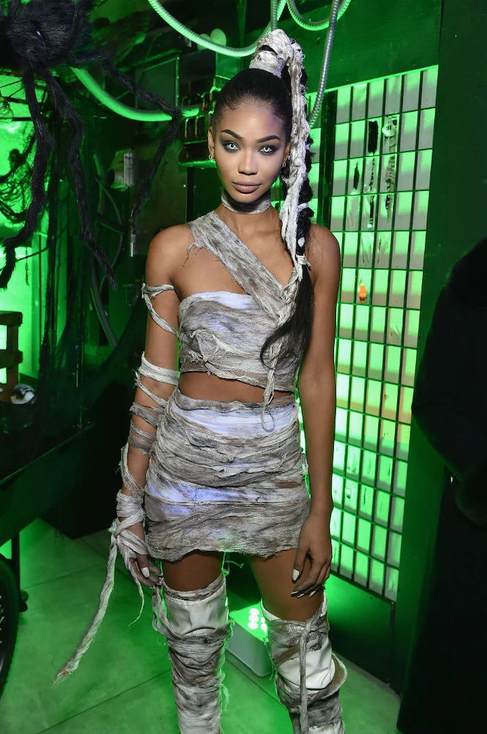 woman dressed as a mummy, adult halloween costumes, wearing contact lenses, braided ponytail, neon background