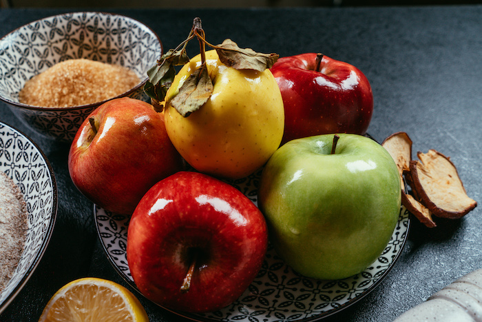 red green and yellow apples in black and white plate, apple pie recipe, placed on black surface