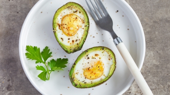 halved avocados, baked with eggs inside, on white plate, breakfast potluck
