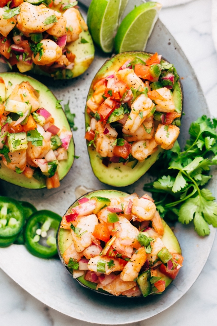 halved avocado, filled with shrimp, peppers and onion, breakfast recipes, on white plate