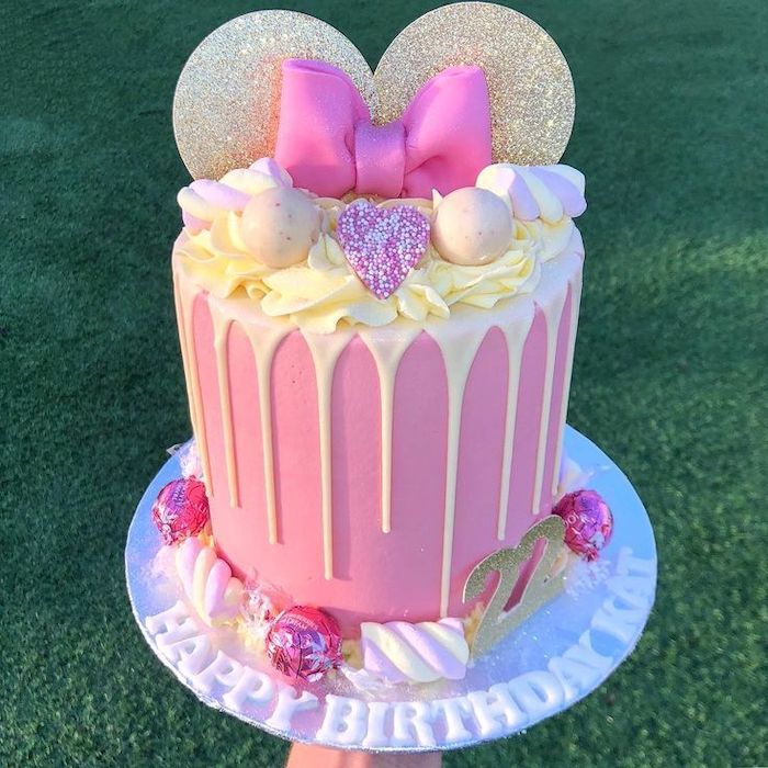 white cake stand, minnie mouse birthday cake, pink fondant, candy decorations, gold ears, pink bow, red and black minnie mouse cake