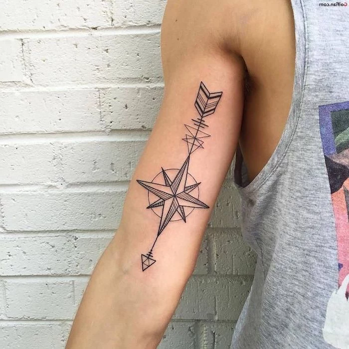 inside arm tattoo, compass rose tattoo, white brick wall, man with grey t shirt