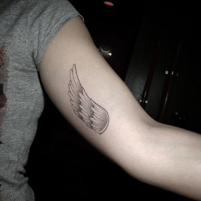 inside arm tattoo, woman with grey top, black background, angel wings tattoo on back