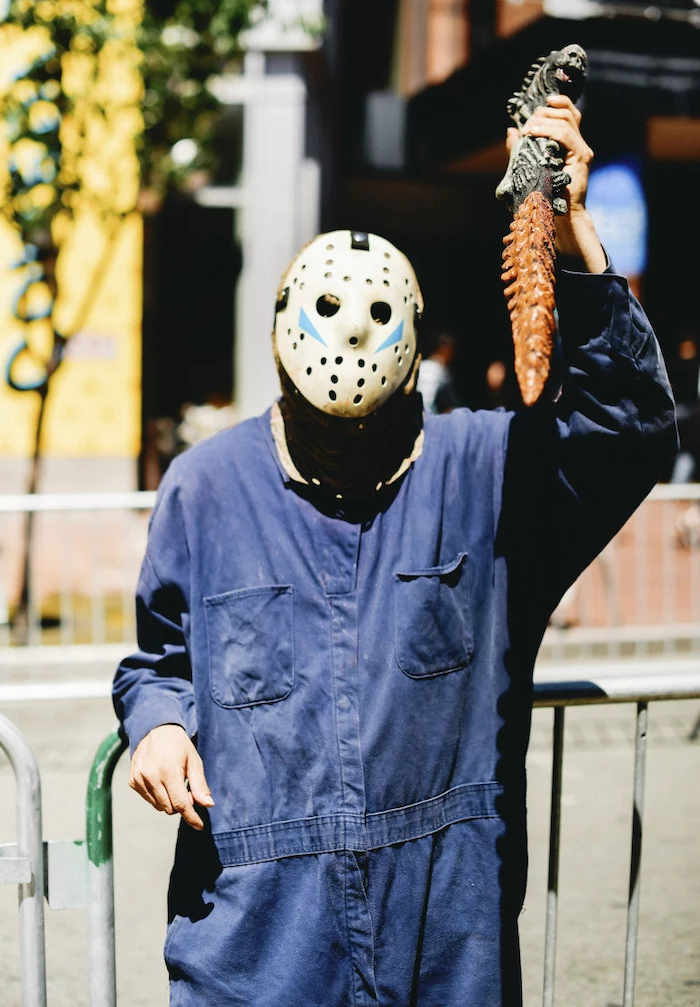 man dressed as jason voorhees, simple halloween costumes, blue onesie, holding a weapon, hockey mask