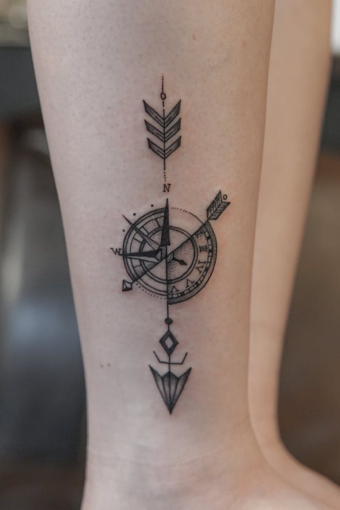 compass tattoos for men, leg tattoo, half compass, half watch, arrow going through the middle, blurred background
