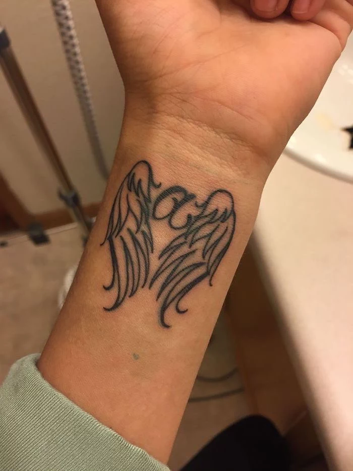 wrist tattoo, letter a, between two angel wings, angel sleeve tattoo, blurred background, angel and demon wing back tattoos