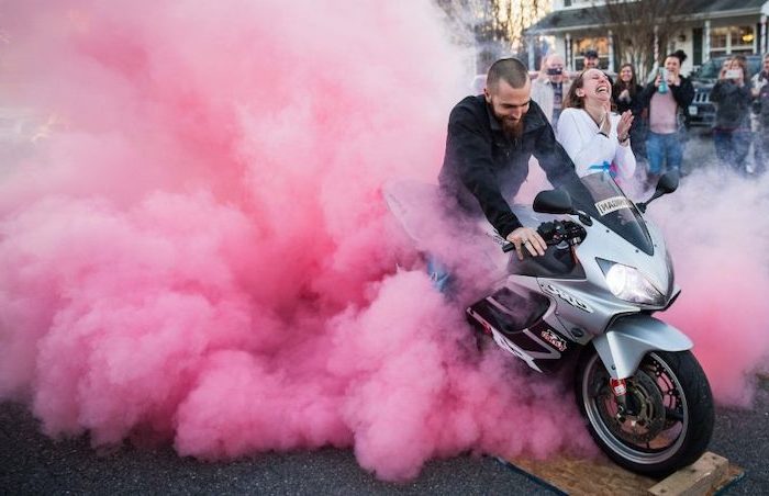 man on a motorcycle, blowing pink smoke, gender reveal party, woman smiling
