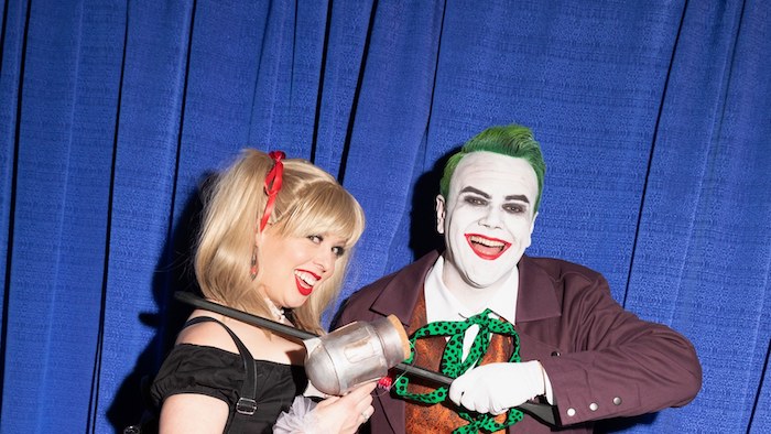 the joker and harley quinn, creative halloween costumes, man and woman smiling, standing in front of a blue curtain