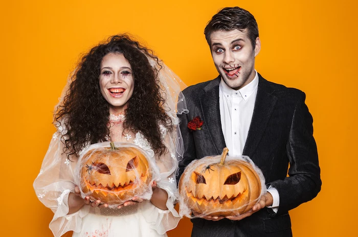 man and woman smiling, holding pumpkins, dressed as bride and groom, diy halloween costumes, orange background