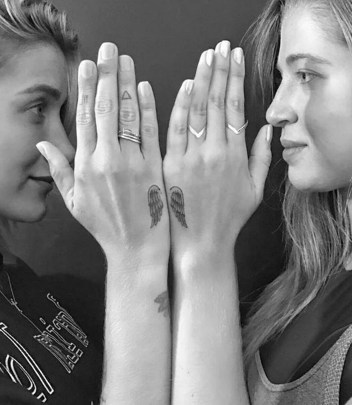matching sister tattoos, hand tattoos, angel sleeve tattoo, two women, facing each other, silver rings