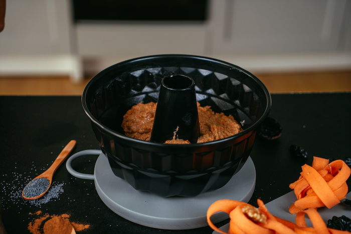 cake mixture transferred to a bundt cake pan, placed on grey board, carrot cake recipe, placed on black table