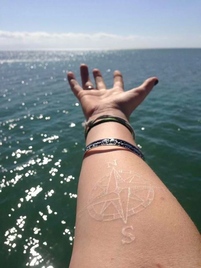 compass meaning, white tattoo, forearm tattoo, sea waves, hand with bracelets