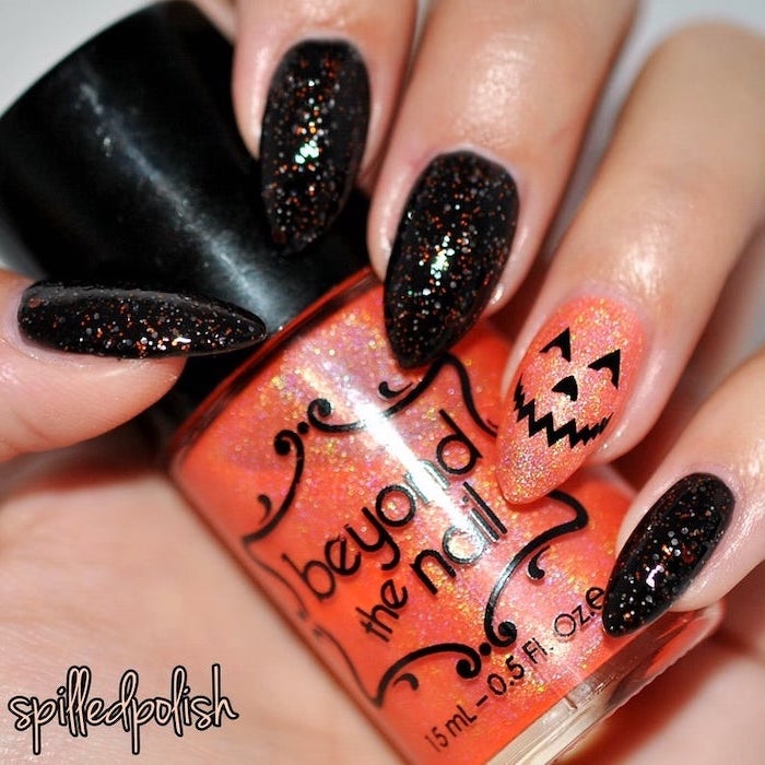 cute acrylic nail ideas, black and orange, glitter nail polish, almond nails, holding an orange glitter nail polish