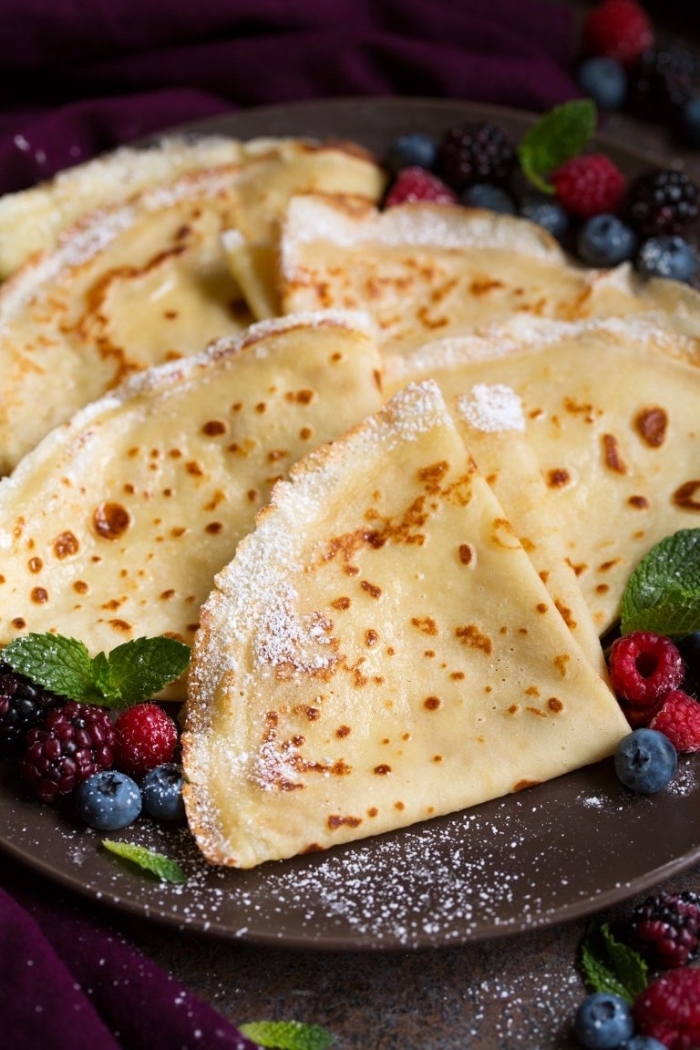 folded pancakes, powdered sugar, blueberries and raspberries, breakfast and brunch, black plate